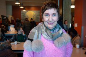 femme avec chandail rose et écharpe dans une salle pleine de gens